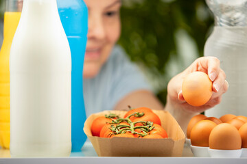 View from inside the fridge as a woman reaches for an egg. Healthy groceries including tomatoes, milk, and drinks. Domestic food scene and kitchen lifestyle.