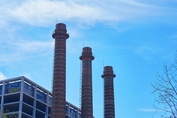 Red brick industrial chimneys against blue sky next to graffiti-covered building
