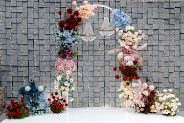 Wedding arch decorated with colorful flowers and chandeliers illuminating the gray stone wall