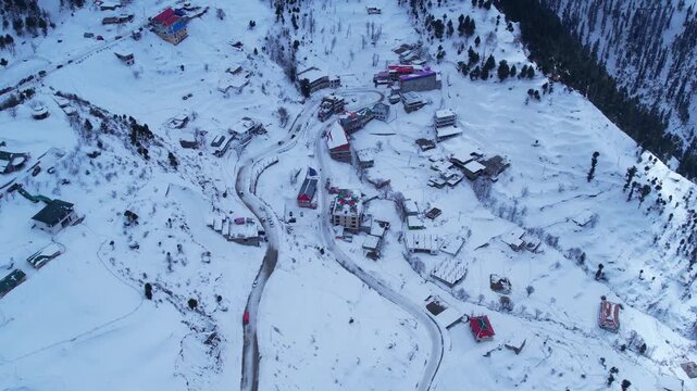 Aerial shot panning up a snowy mountain village, revealing a majestic hotel and the expansive winter landscape. Malam Jabba hill station.