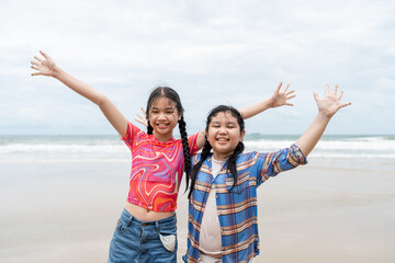 Two young girls joyfully smiling and raising their arms on the beach after playing in the sea....