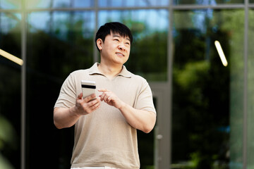 Asian man using smartphone and credit card for online shopping near modern building