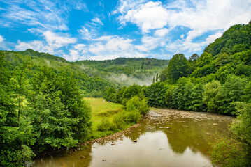 Lush green landscape with a winding river flowing through hills under a bright blue sky