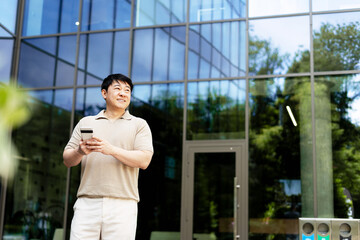 Asian businessman using smartphone in front of modern office building