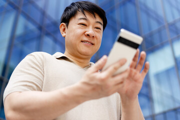 Asian businessman using smartphone in front of modern office building
