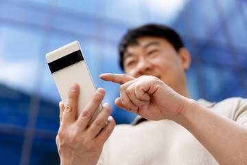Asian businessman using mobile phone app in front of modern office buildings