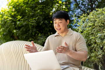 Asian man having video call on laptop in a park