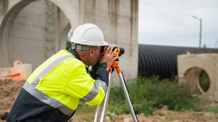 The survey team is using a theodolite and road construction plans. Civil engineers are measuring...