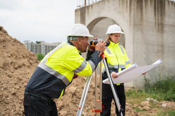 The survey team is using a theodolite and road construction plans. Civil engineers are measuring with surveying tools during the construction