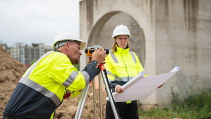 The survey team is using a theodolite and road construction plans. Civil engineers are measuring...