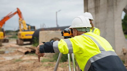 The survey team is using a theodolite and road construction plans. Civil engineers are measuring with surveying tools during the construction