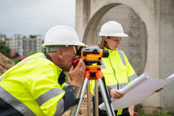 The survey team is using a theodolite and road construction plans. Civil engineers are measuring with surveying tools during the construction
