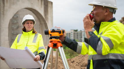 The survey team is using a theodolite and road construction plans. Civil engineers are measuring...