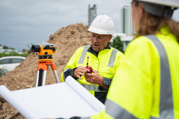 The survey team is using a theodolite and road construction plans. Civil engineers are measuring...