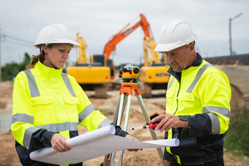 The survey team is using a theodolite and road construction plans. Civil engineers are measuring with surveying tools during the construction