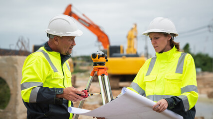 The survey team is using a theodolite and road construction plans. Civil engineers are measuring...