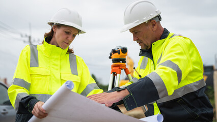 The survey team is using a theodolite and road construction plans. Civil engineers are measuring with surveying tools during the construction