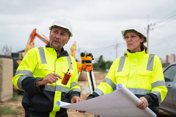 The survey team is using a theodolite and road construction plans. Civil engineers are measuring with surveying tools during the construction