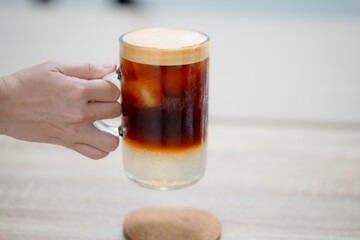 Close up and selective forcus hand holding glass of iced espresso in the morning.