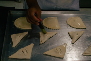 A chef brushes egg wash onto freshly prepared pastry dough in a busy kitchen environment, ready for...