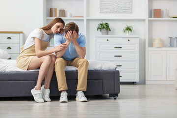 Young woman apologizing to her frustrated boyfriend on bed at home