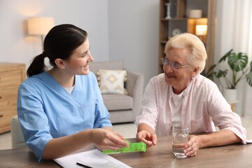 Nurse giving pills to senior woman at wooden table indoors. Home health care service