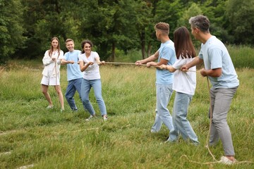 Team building. Group of happy people playing tug of war with rope outdoors