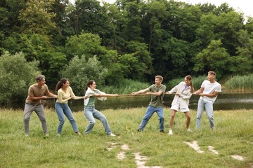 Team building. Group of happy people playing tug of war with rope outdoors