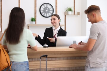Smiling receptionist in uniform with hotel key card working with clients at reception desk indoors