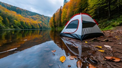 A white and red camping tent sits by a serene lake surrounded by vibrant autumn foliage, creating a peaceful and picturesque outdoor setting.,camping tent