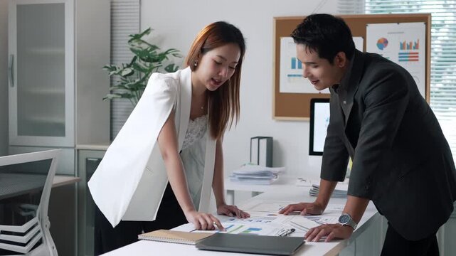 Professional business partners collaborating, strategizing, and finalizing project details through engaging discussion, handshake, and joint analysis in contemporary office workspace
