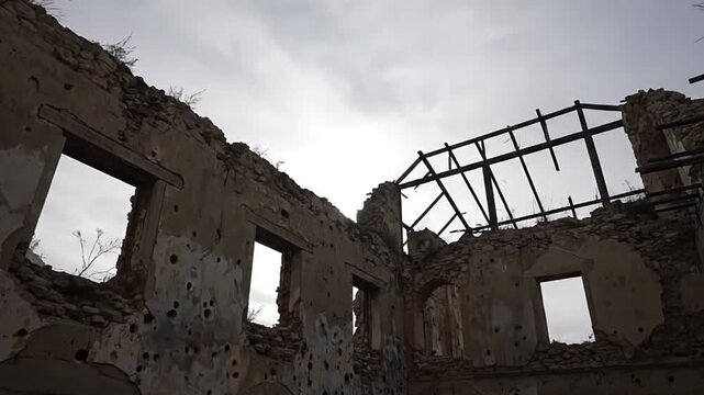 A ruined stone building stands against a cloudy sky marked with holes and missing portions The skeletal remains of its roof are visible