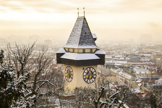 View of the iconic clock tower, snow-dusted and standing tall amidst a winter landscape, a beacon against the hazy horizon, Graz, Styria, Austria.