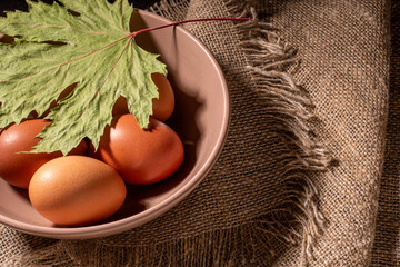Fresh chicken eggs in a bowl decorated with a maple leaf on burlap napkin