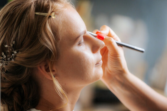 A bride smiles gently as a stylist arranges her hair, capturing a calm and joyful moment of wedding preparation.