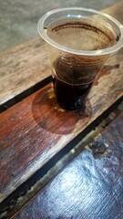 Intimate shot of a glass of hot black coffee placed on a wooden coaster on a wooden table. A plastic cup of coffee.