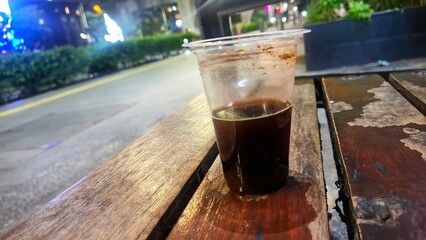 Intimate shot of a glass of hot black coffee placed on a wooden coaster on a wooden table. A...