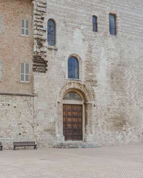 Fototapeta View of an ancient stone building with a dark wooden door, showcasing a blend of textures and architectural details, Gubbio, Umbria, Italy.