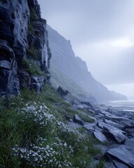 Misty coastal landscape with wildflowers and rocks.
