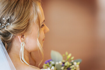 A soft side profile of a bride showing delicate pearl earrings, a crystal hair accessory, and a...