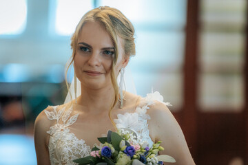 Close-up of a smiling bride in a white lace gown and long earrings, holding a pastel floral bouquet...