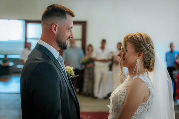 The bride and groom look into each others eyes during their indoor wedding ceremony, surrounded by...