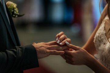 Fototapeta premium A close-up moment of a bride gently placing a gold wedding ring on the groom’s finger during their marriage ceremony. Intimate and symbolic gesture.