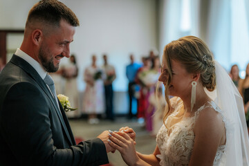 The bride and groom kiss during their indoor wedding ceremony, surrounded by guests in the background. A moment of joy and love.