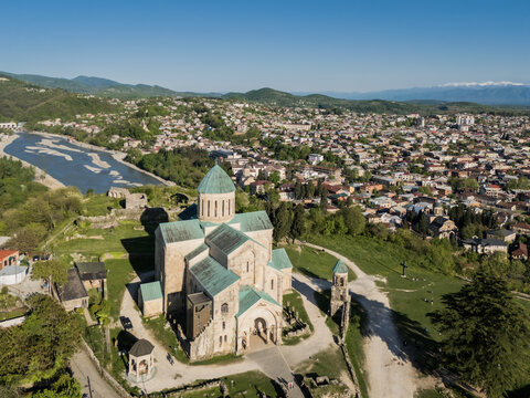 Aerial view of the majestic Bagrati Cathedral stands proudly against the backdrop of Kutaisi's urban sprawl, framed by rolling hills and the Rioni River, Kutaisi, Imereti, Georgia.