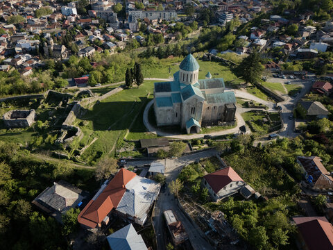 Aerial view of the Bagrati Cathedral stands majestically amidst verdant foliage and ancient ruins, a testament to time and faith, Kutaisi, Imereti, Georgia.