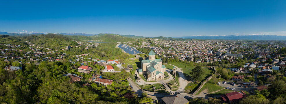 Aerial panoramic view of Bagrati Cathedral stands majestically amidst lush greenery and the Rioni River, with Kutaisi sprawling in the distance, Kutaisi, Imereti, Georgia.
