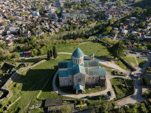 Aerial view of Bagrati Cathedral, with its weathered stone facade and faded teal dome contrasting with the vibrant green landscape, Kutaisi, Imereti, Georgia.