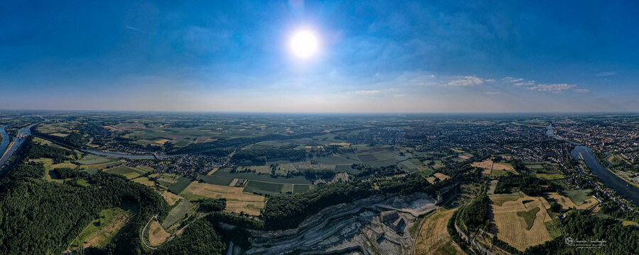 Aerial view of sun-kissed fields meet the meandering river, contrasting with the stark quarry against the backdrop of the town, Valkenburg, Limburg, Netherlands.