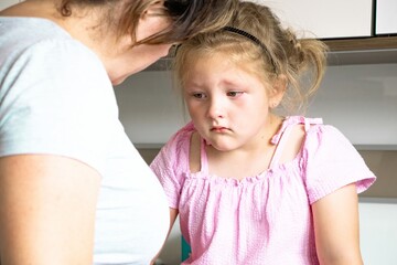 Young girl in pink dress looks down with a concerned expression while an adult woman leans in,...